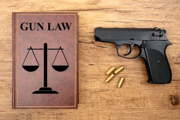 a Book Titled'gun law' is sitting on a table beside a gun and four bullets