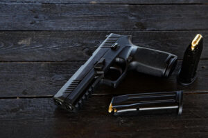 A small black pistol and two magazines placed on a dark wooden table - Eastern Gun Expo a Small Black Pistol and Two Magazines Placed on a Dark Wooden Table