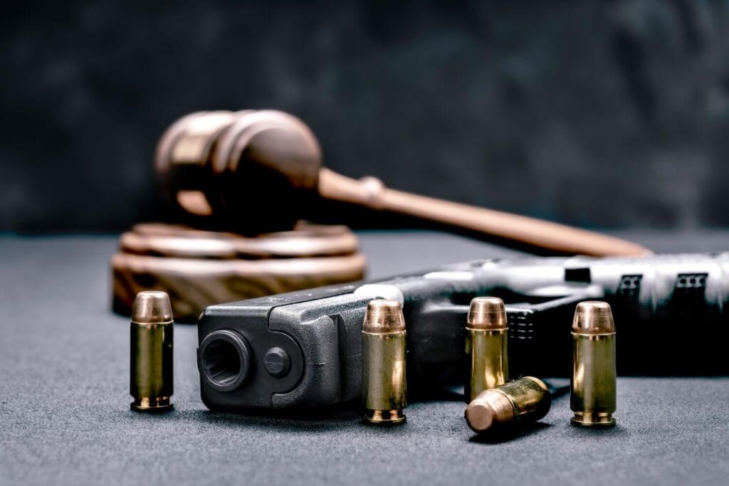 a Black Pistol and Five Bullets Are Laying on a Black Table Next to a Gavel