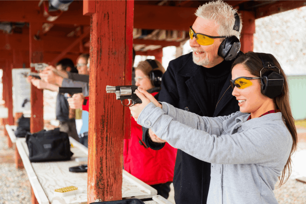 A man and a woman at a gun range wearing protective ear and eye wear. The woman is holding a firearm
