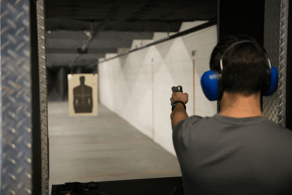 a Man Wearing Blue Ear Protection  Aiming a Firearm at a Paper Target with an Upper Torso Silhouette on It