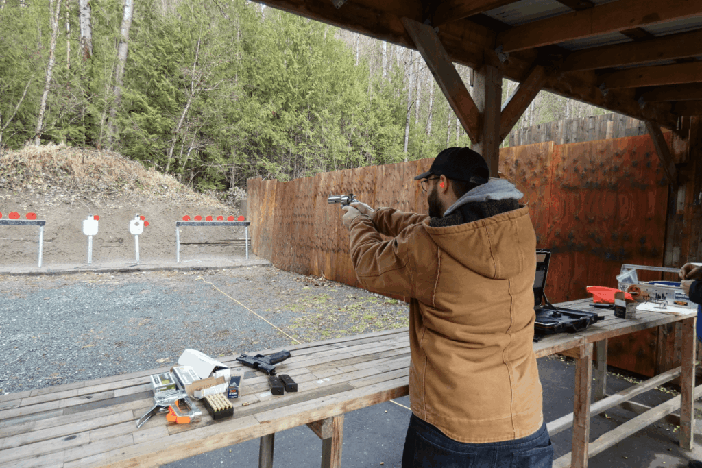 an Outdoor Shooting Range with a Man in a Tan Coat Aiming His Firearm at a Target