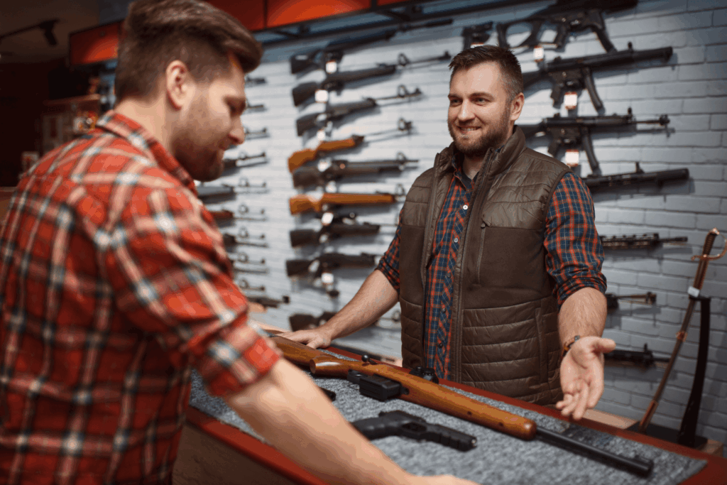 Two men standing at a booth during a gun show with various guns on the table and displayed behind them