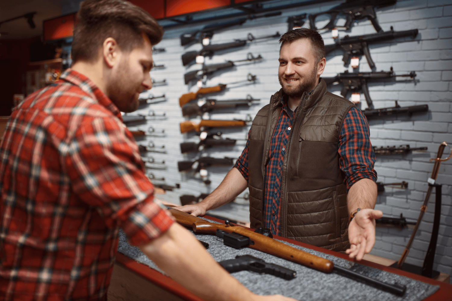 Two Men Standing at a Booth During a Gun Show with Various Guns on the Table and Displayed Behind Them