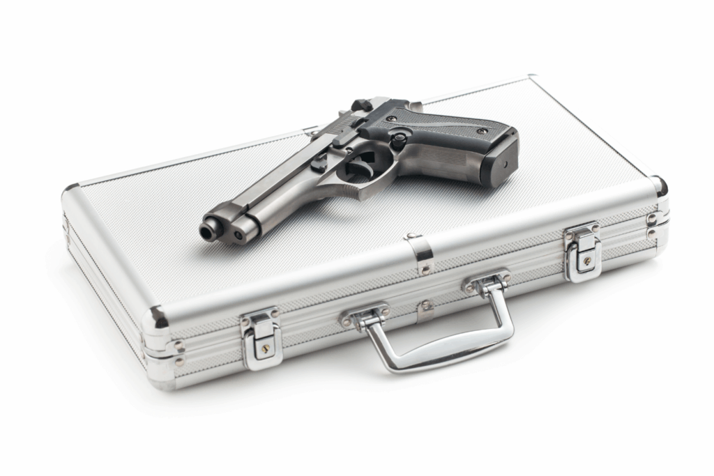 A large, hard silver gun case closed with a gun lying on top of it